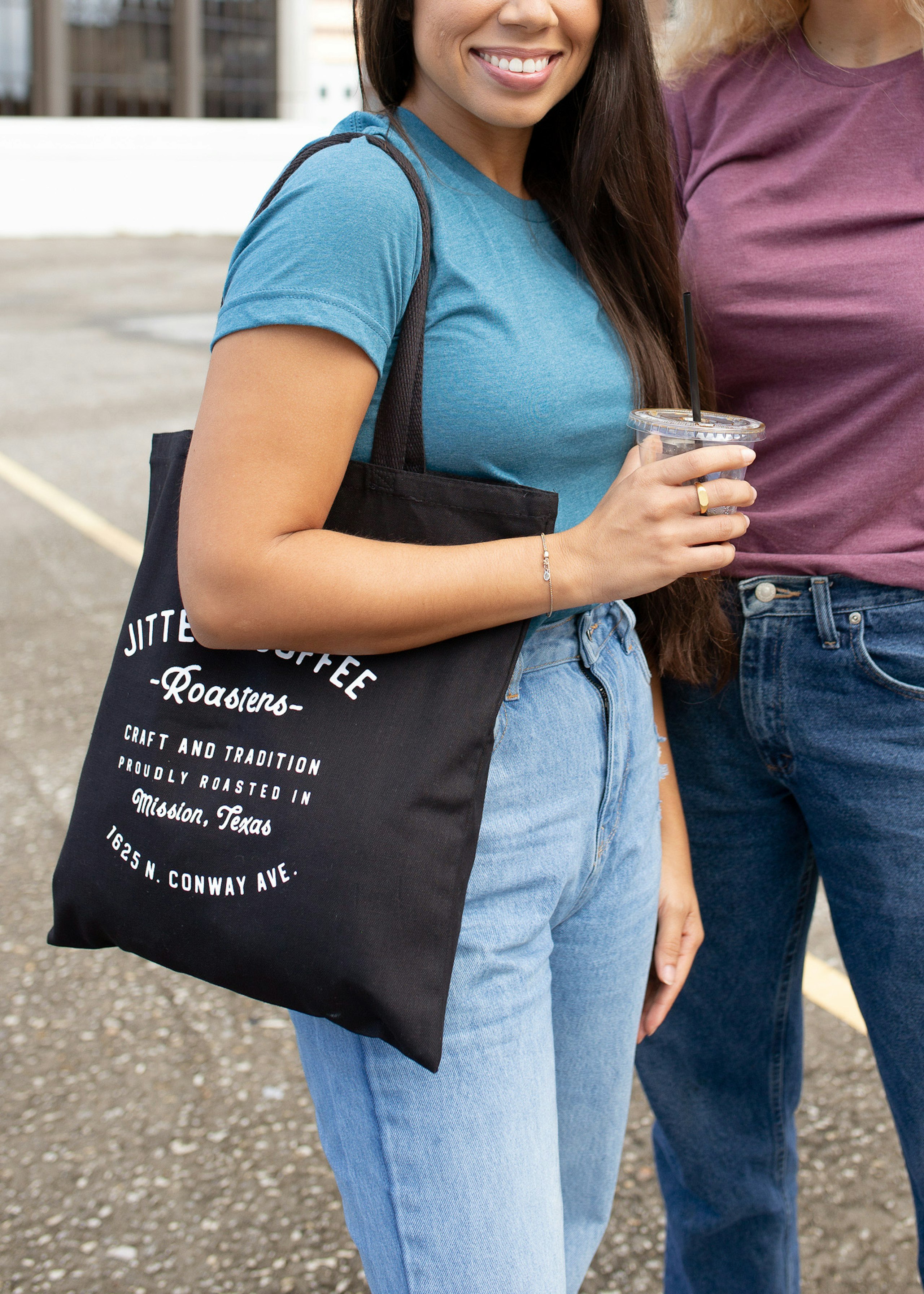 A woman wears a coffee tote bag while holding a cup on the go