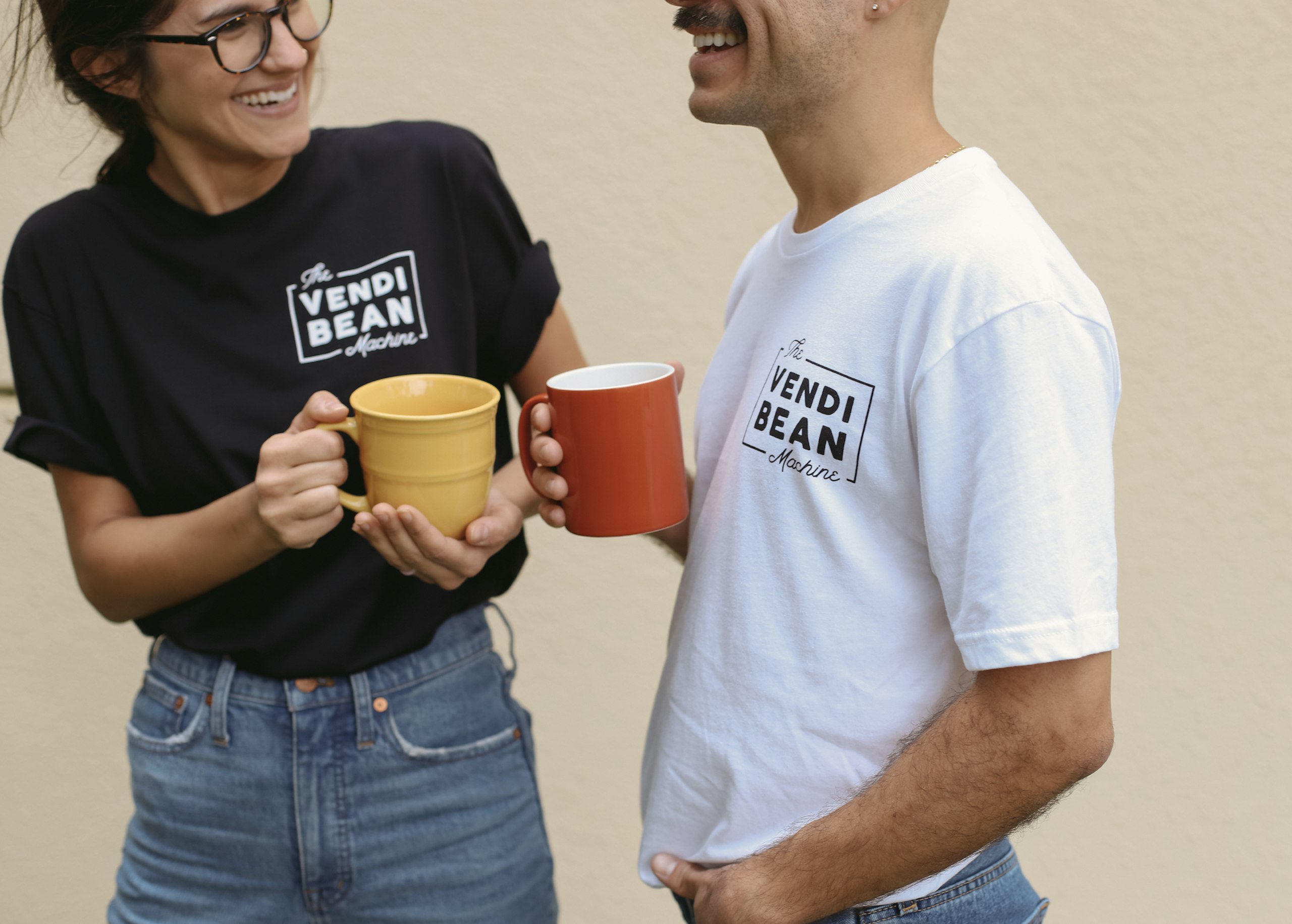 A woman and a man in matching coffee shirts cheers each other with their mugs