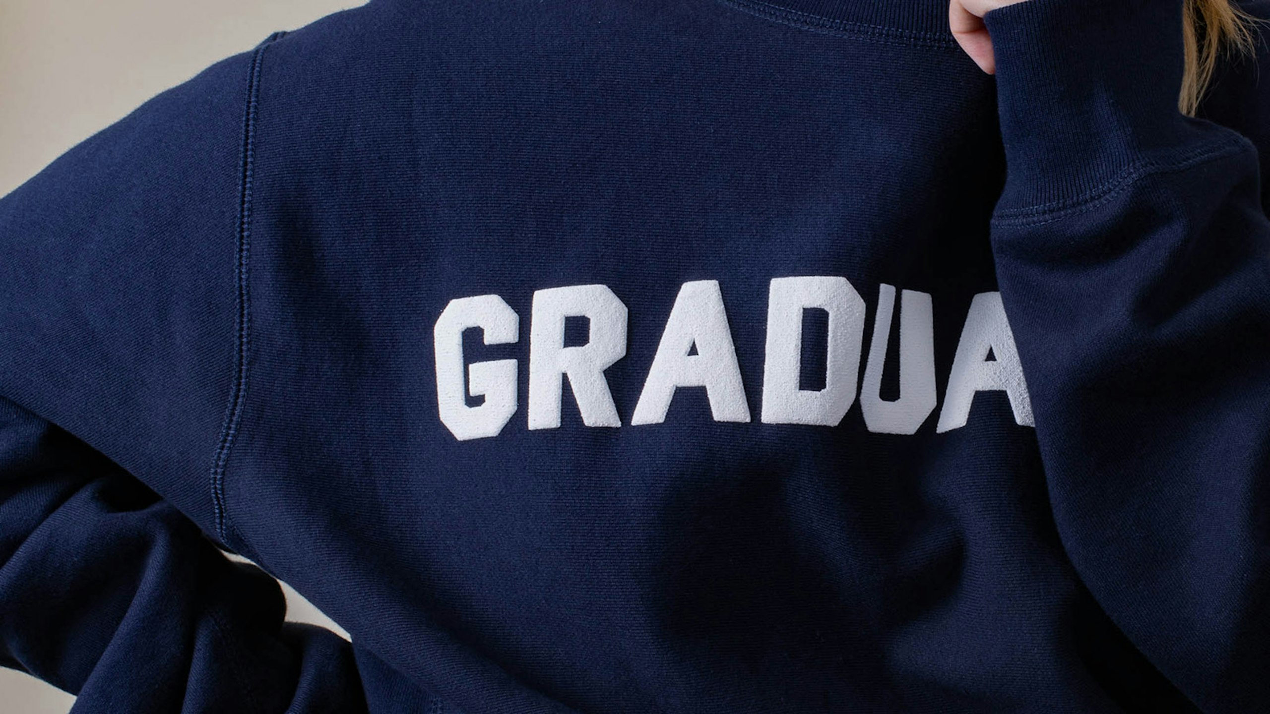 Close up a puff print on a navy hoodie. The letters G, R, A, D, and U are visible. 