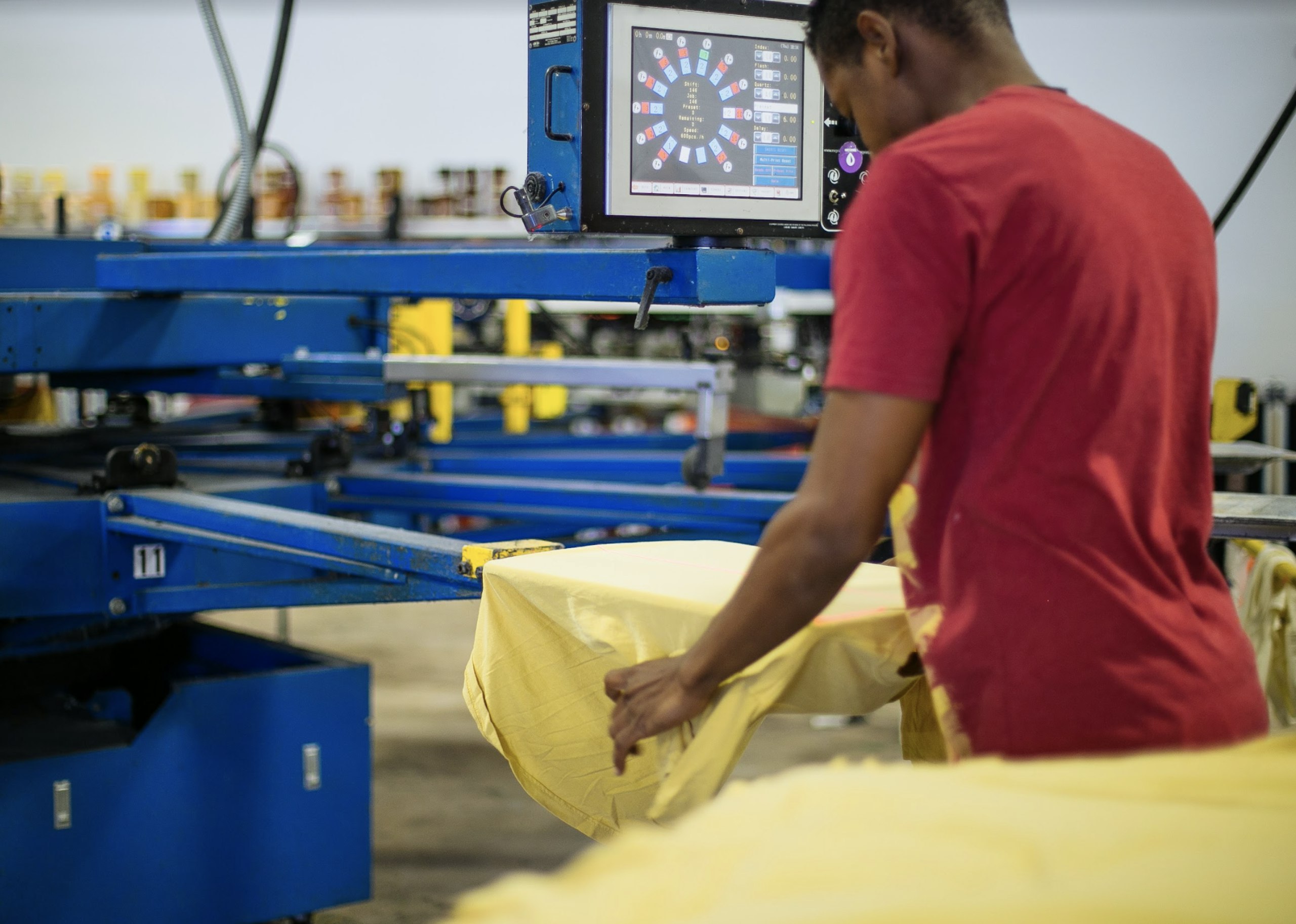 A man loads yellow t-shirts onto a printing press to be custom printed