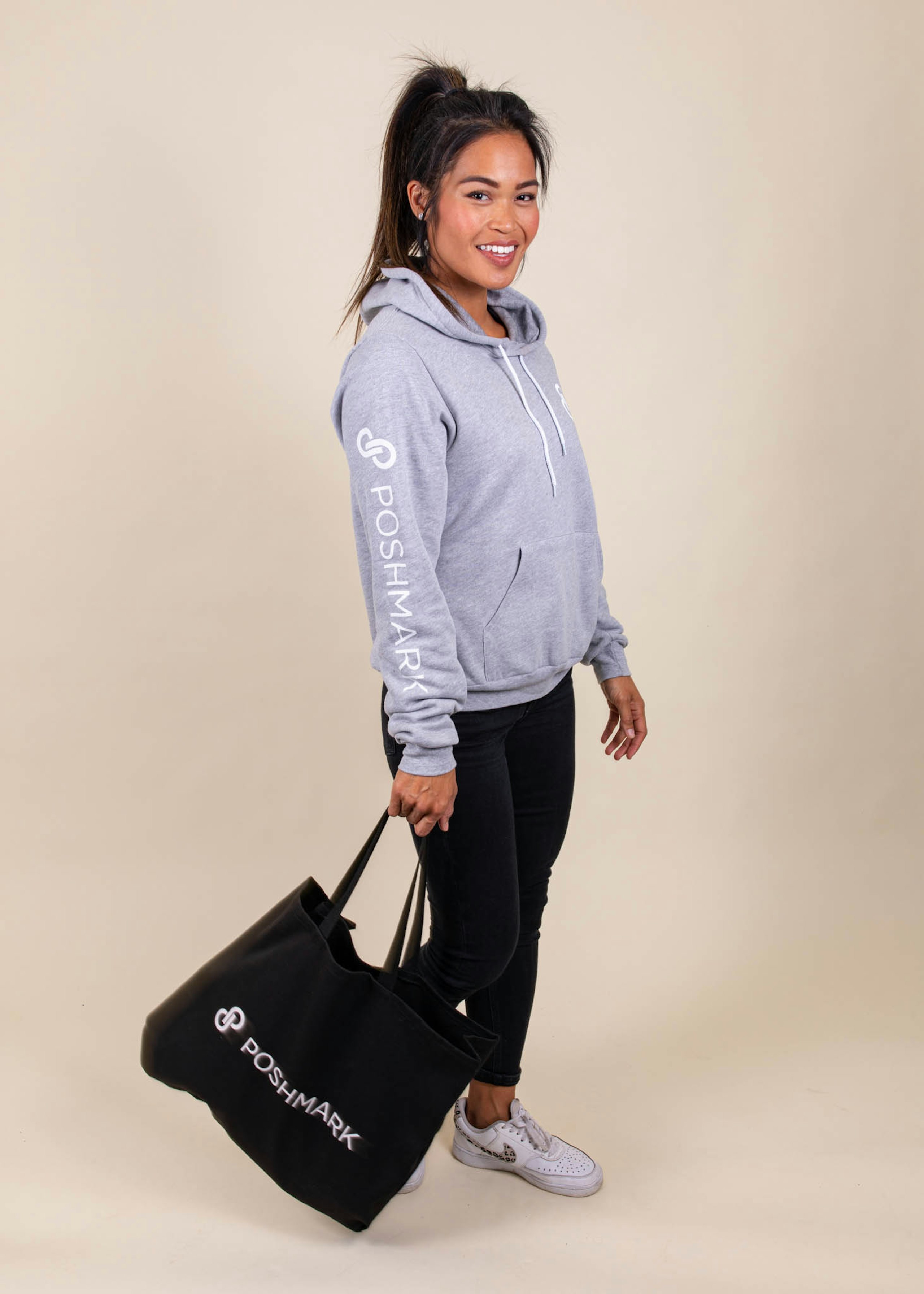 A woman wears a Poshmark sweatshirt and a matching Poshmark tote bag