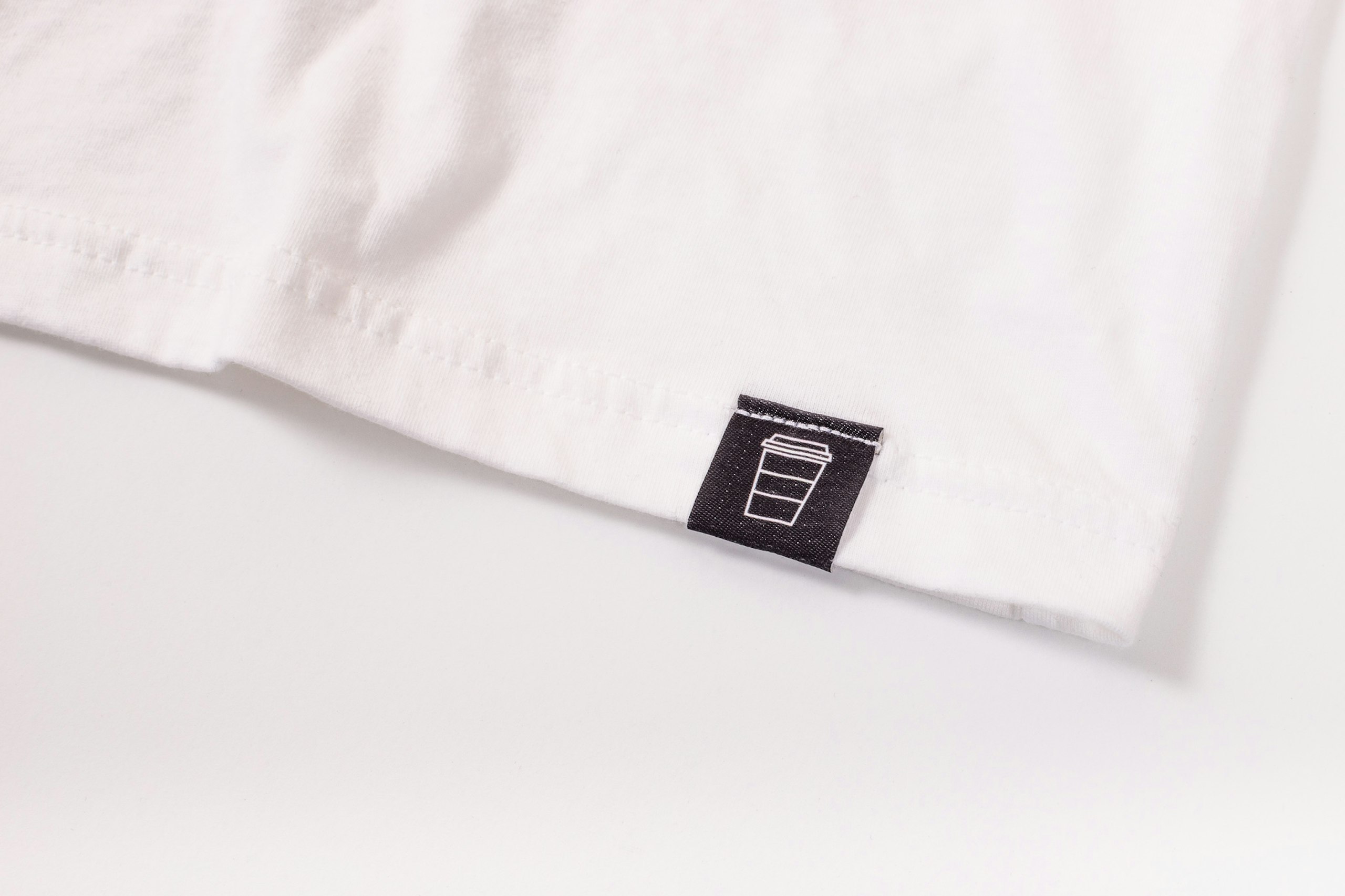A white t-shirt with a black hem tag that has a coffee cup logo on it