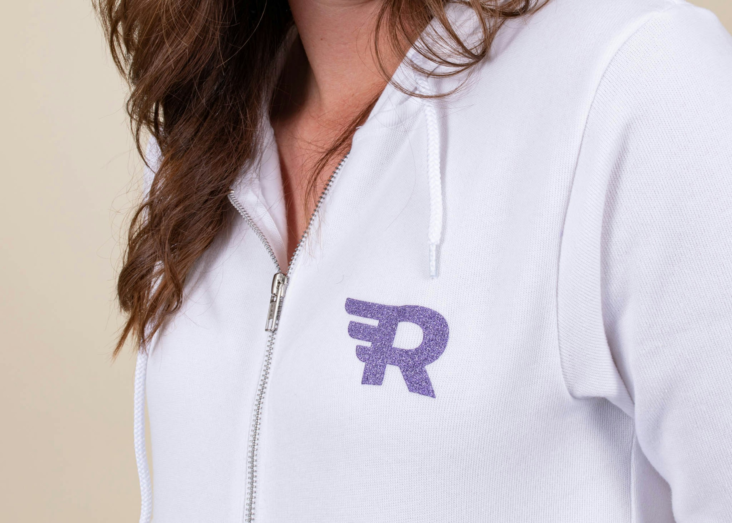 A girl wears a white sweatshirt with an "R" logo in purple metallic ink