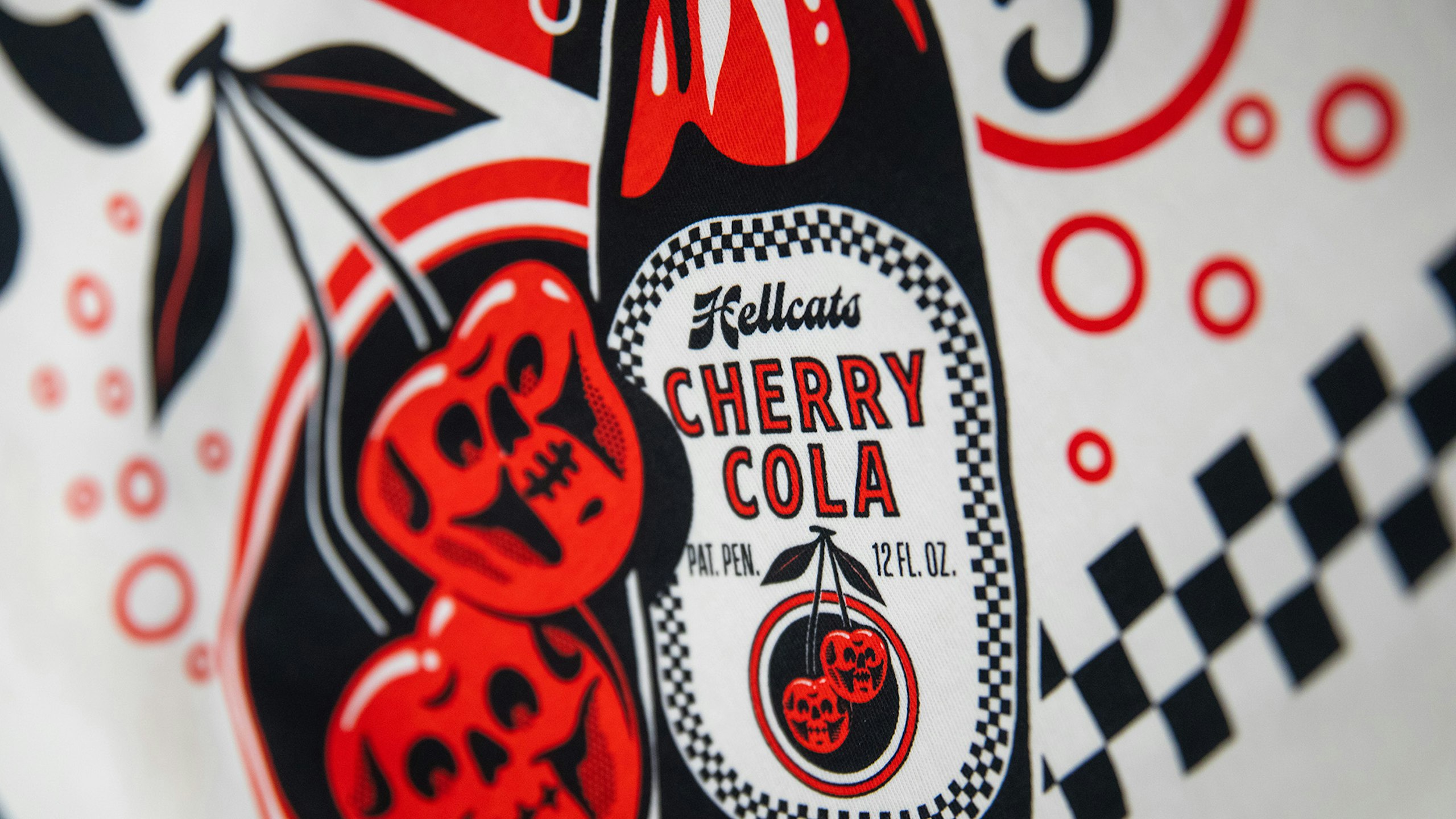 close up of a hellcats design of a cherry cola bottal on a white tee