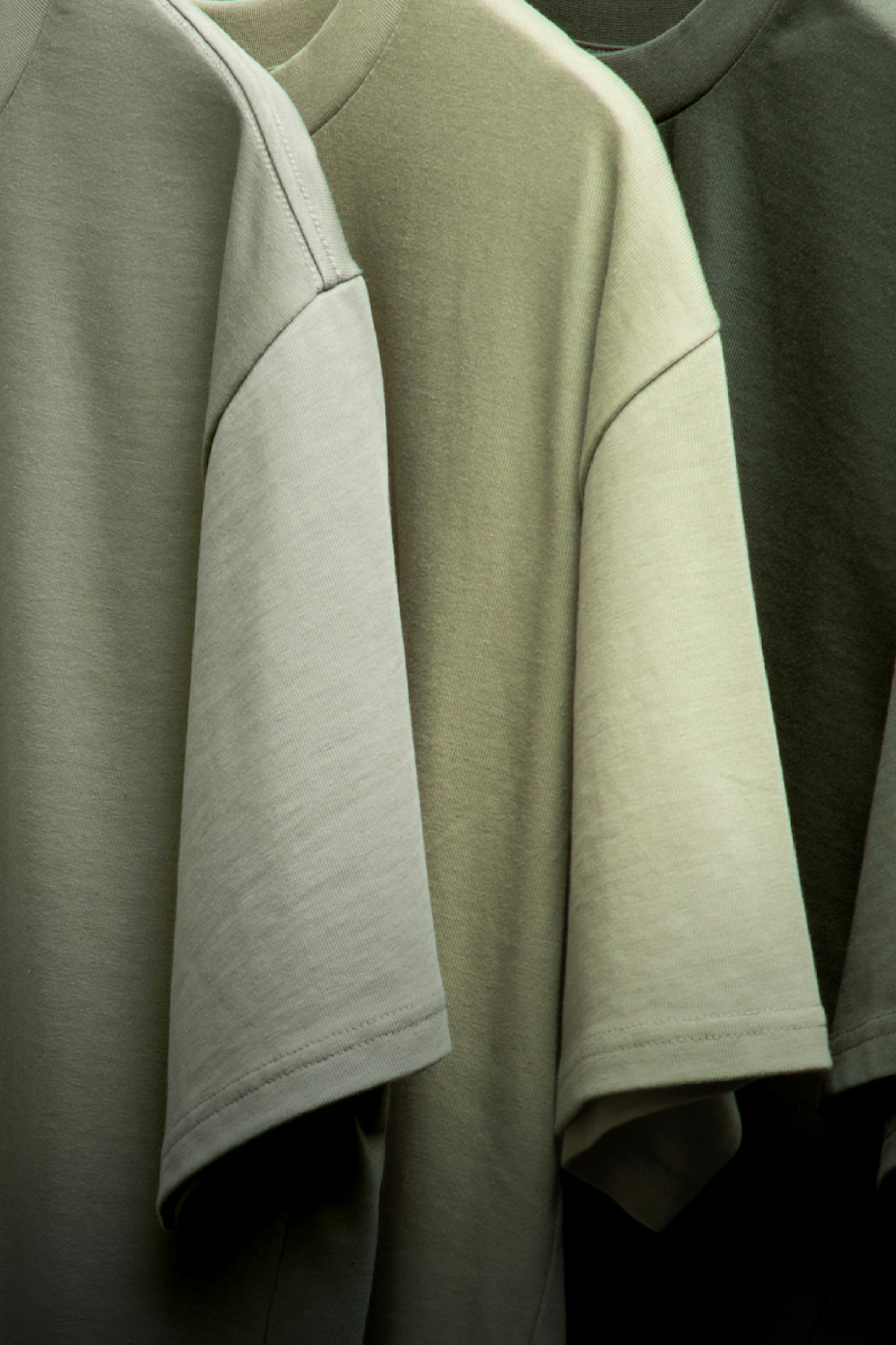 close up of three green t-shirts hanging up