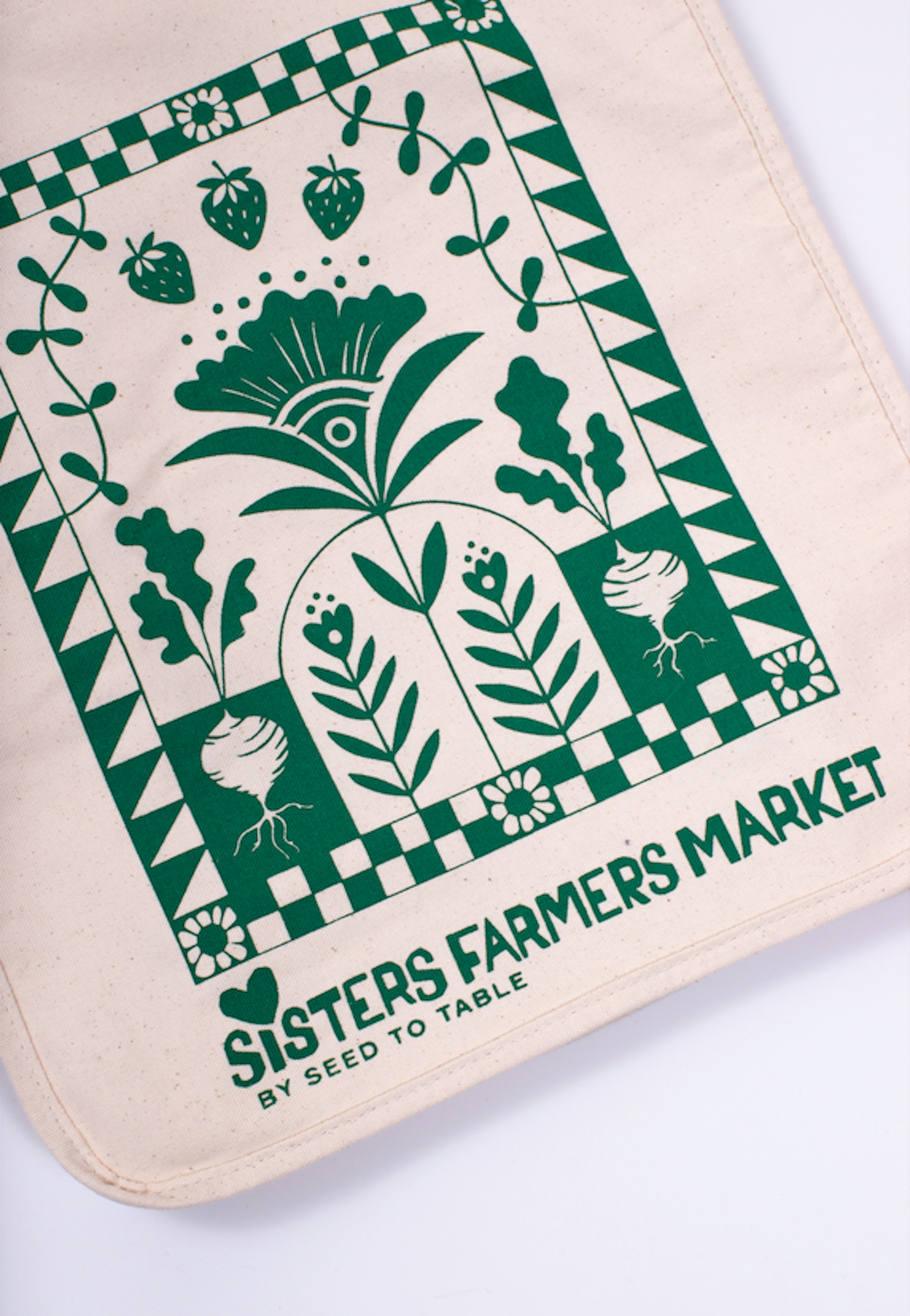 a tote bag printed with green ink with an earthy design and text that says "Sisters Farmers Market"