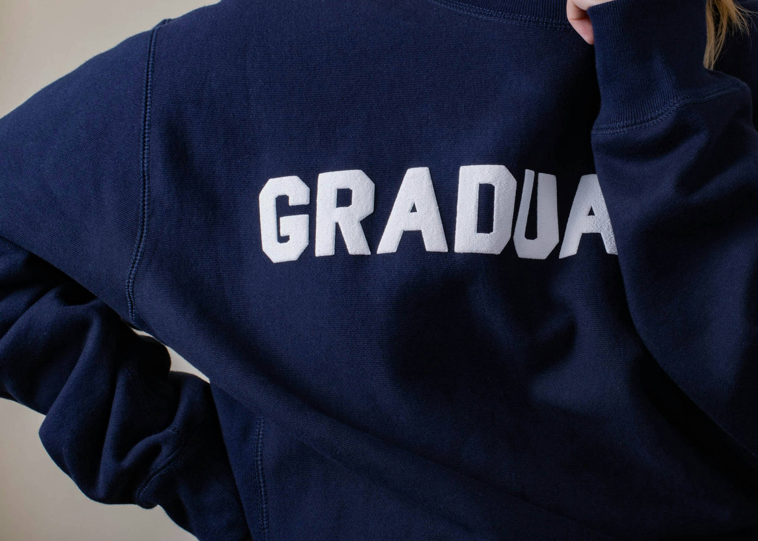 A girl wears a puff ink printed sweatshirt with "Graduate" in white 