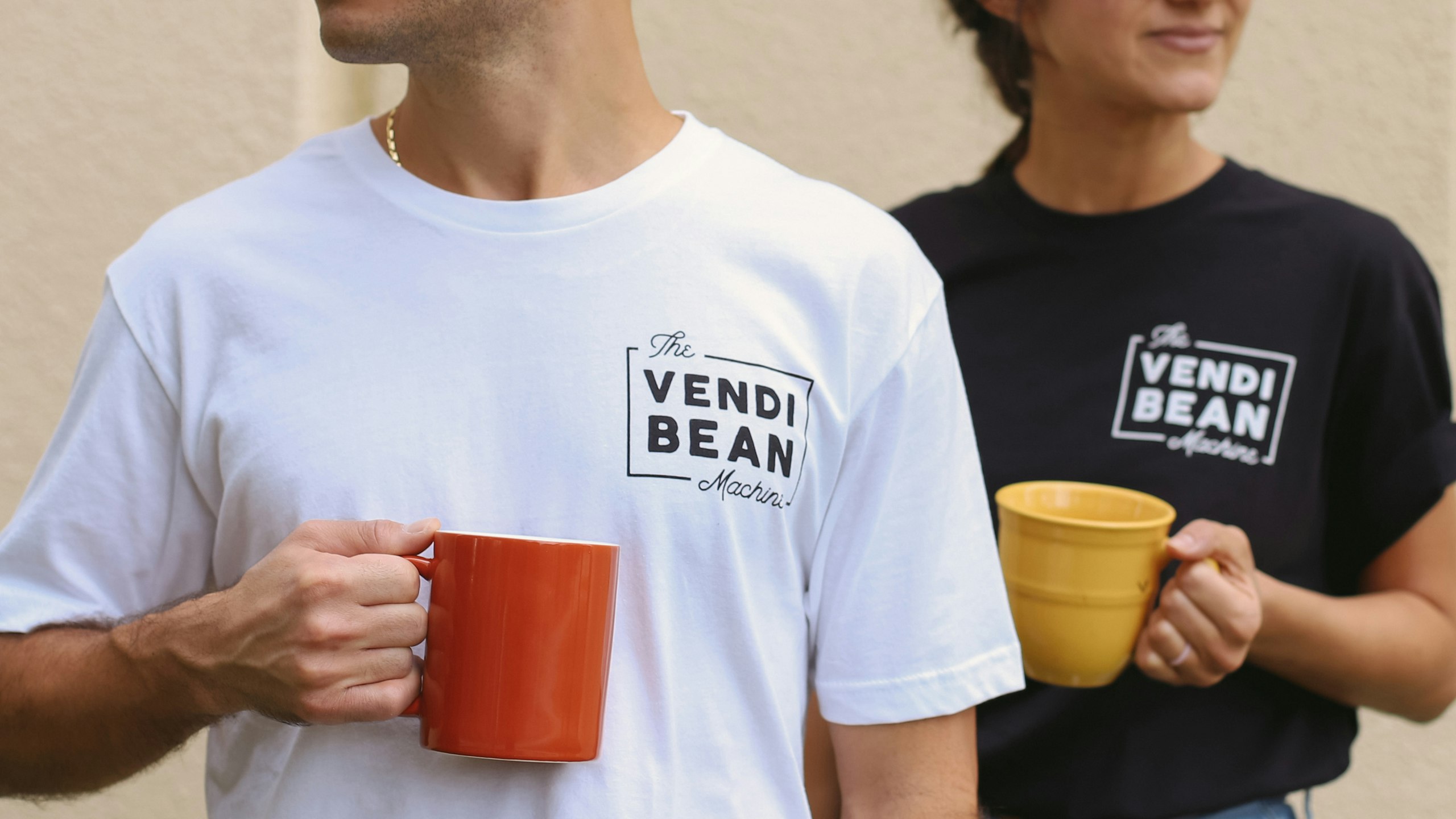 a man and women holding coffee cups with vendi bean t-shirts