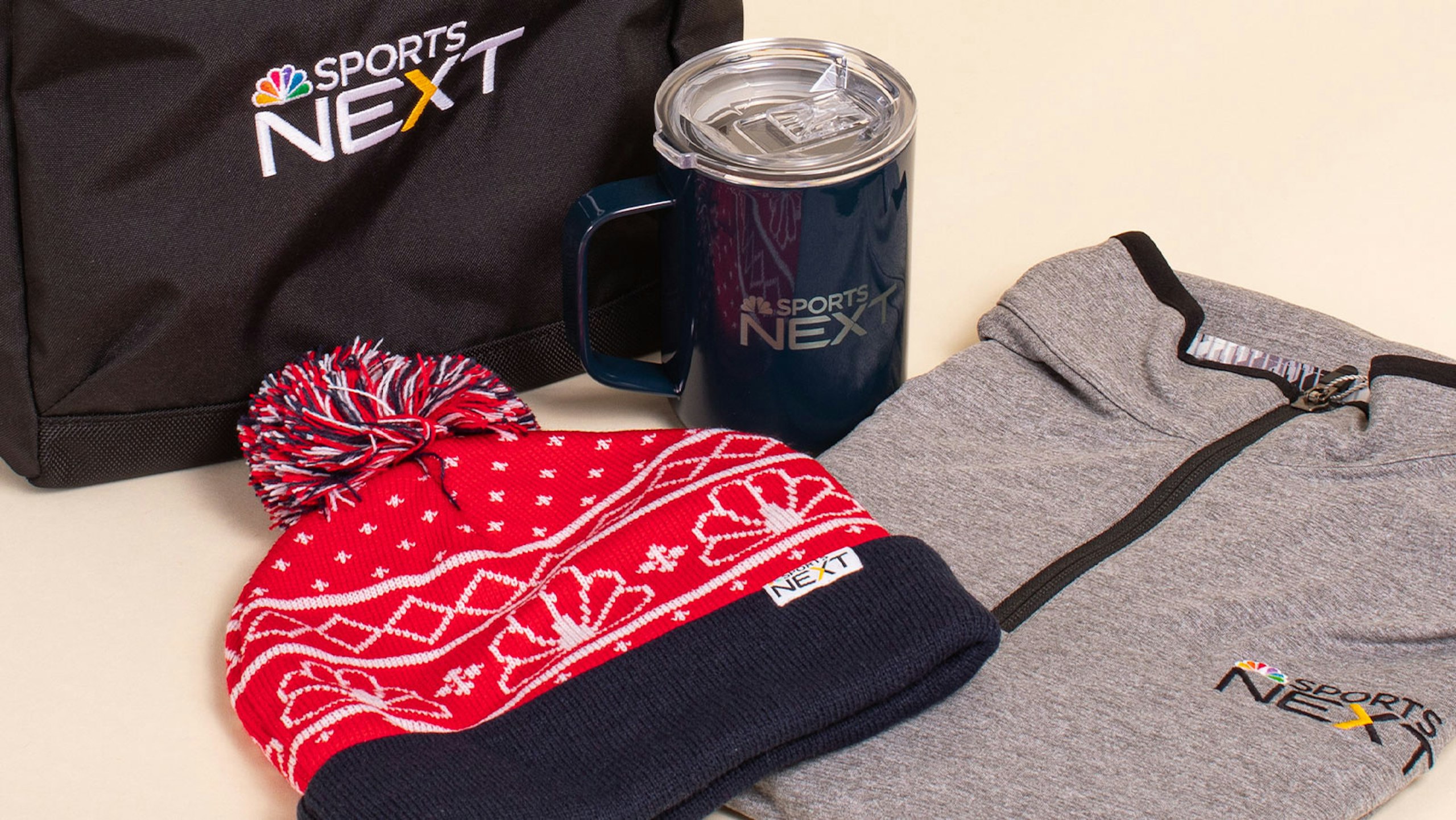 collection of gifts, beanie hat, quarter-zip sweatshirt, cup, and cooler bag