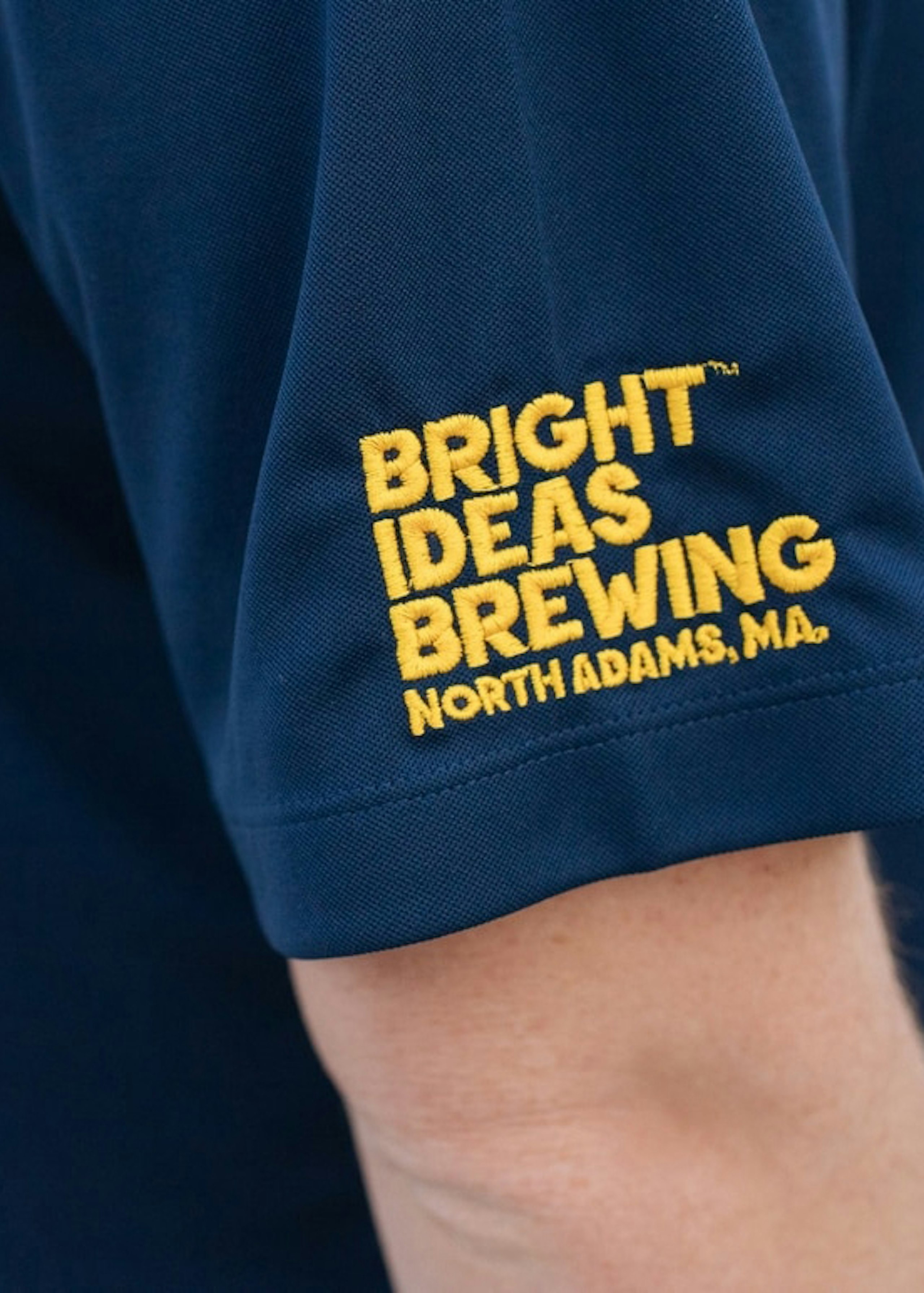 close-up on the sleeve of a polo that is embroidered with yellow text