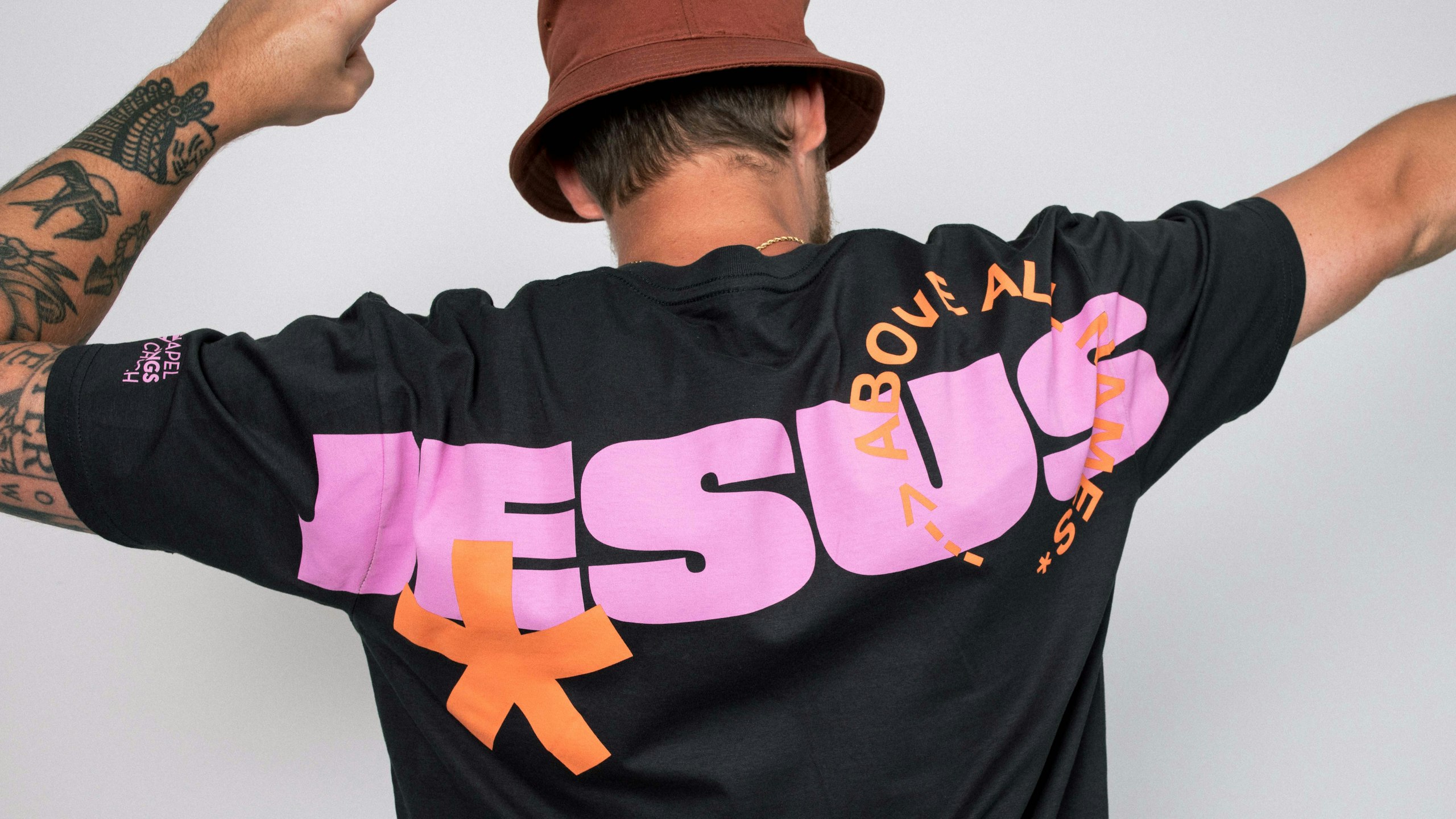 man wearing a black t-shirt with the word Jesus printed large on the back in pink ink
