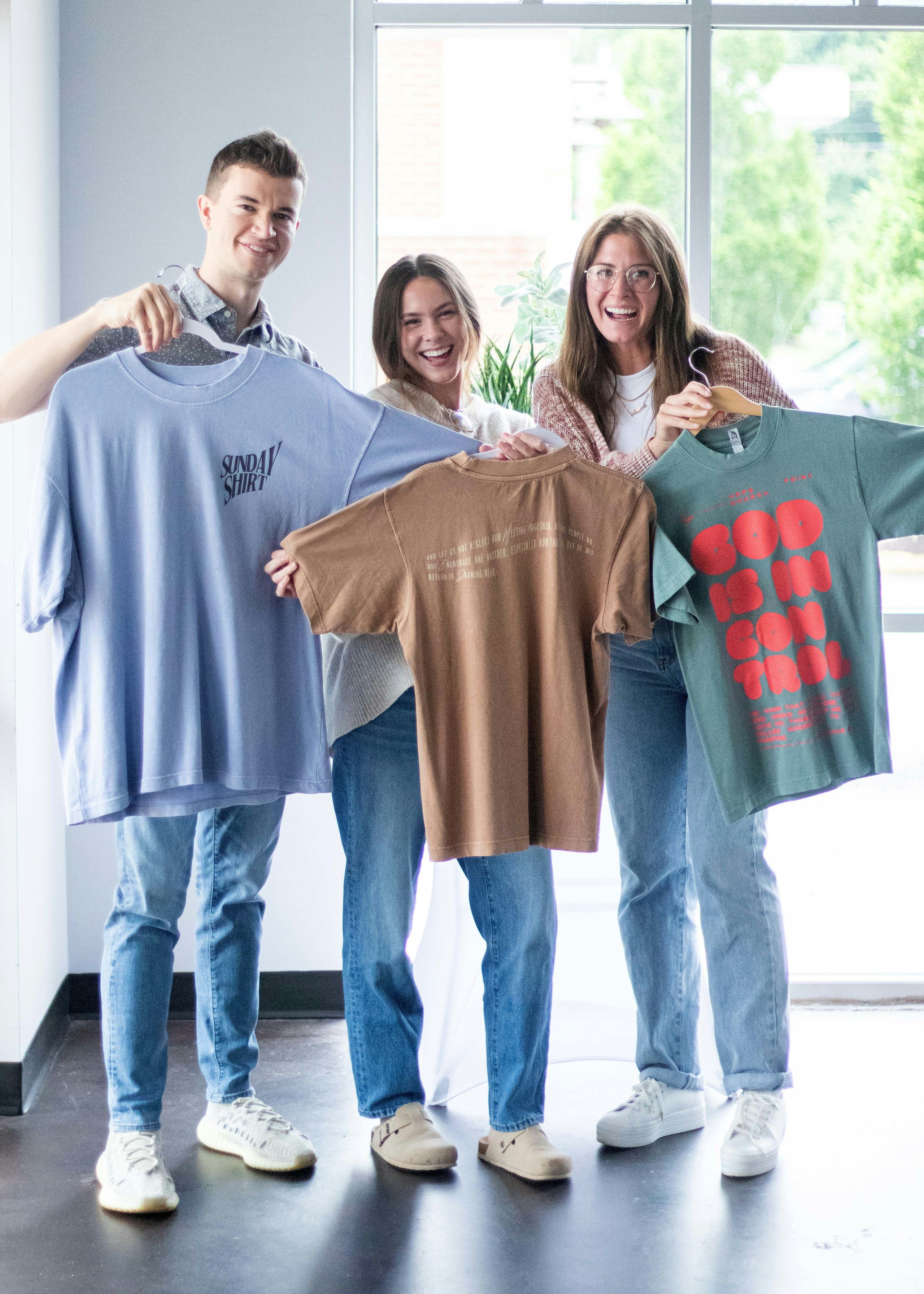 three people holding three different color boxy t-shirts