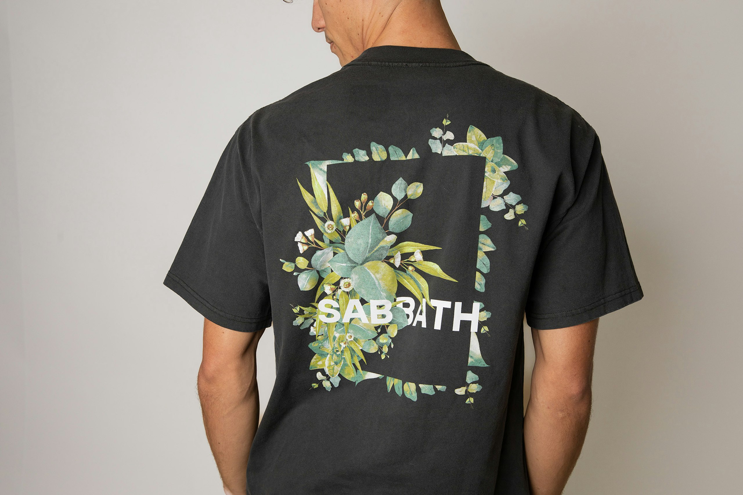 the back of a man wearing a black t-shirt with leaves and the word sabbath screen printed